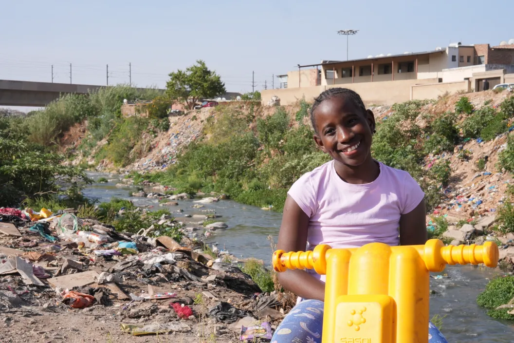 10 year-old Ompfuna Nkhumeleni poses for a portrait, sitting on her plastic motorbike beside the polluted Juskei river. 