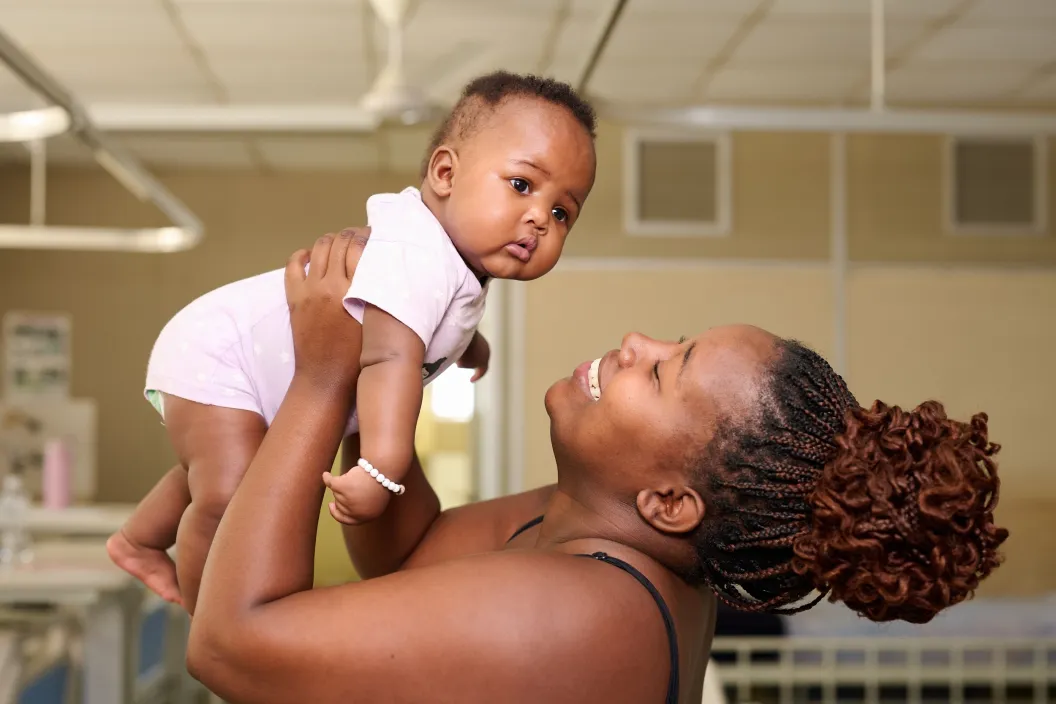 A woman lifts her little baby into the air, smiling happily.