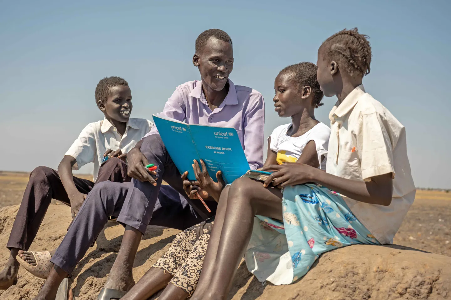 children are sitting and reading a book with their teacher.
