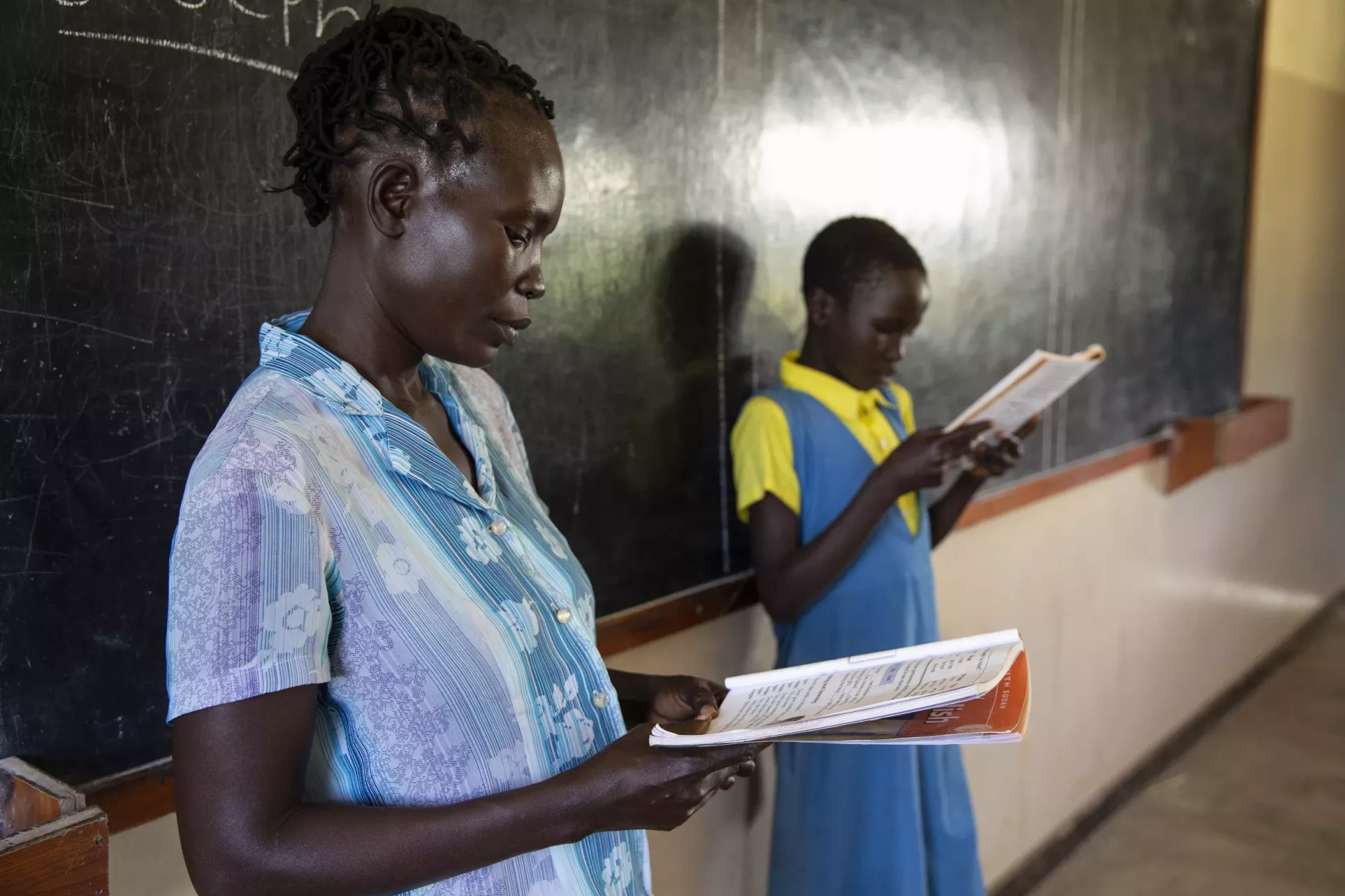 A teacher is photographed reading a book with a student in the classroom