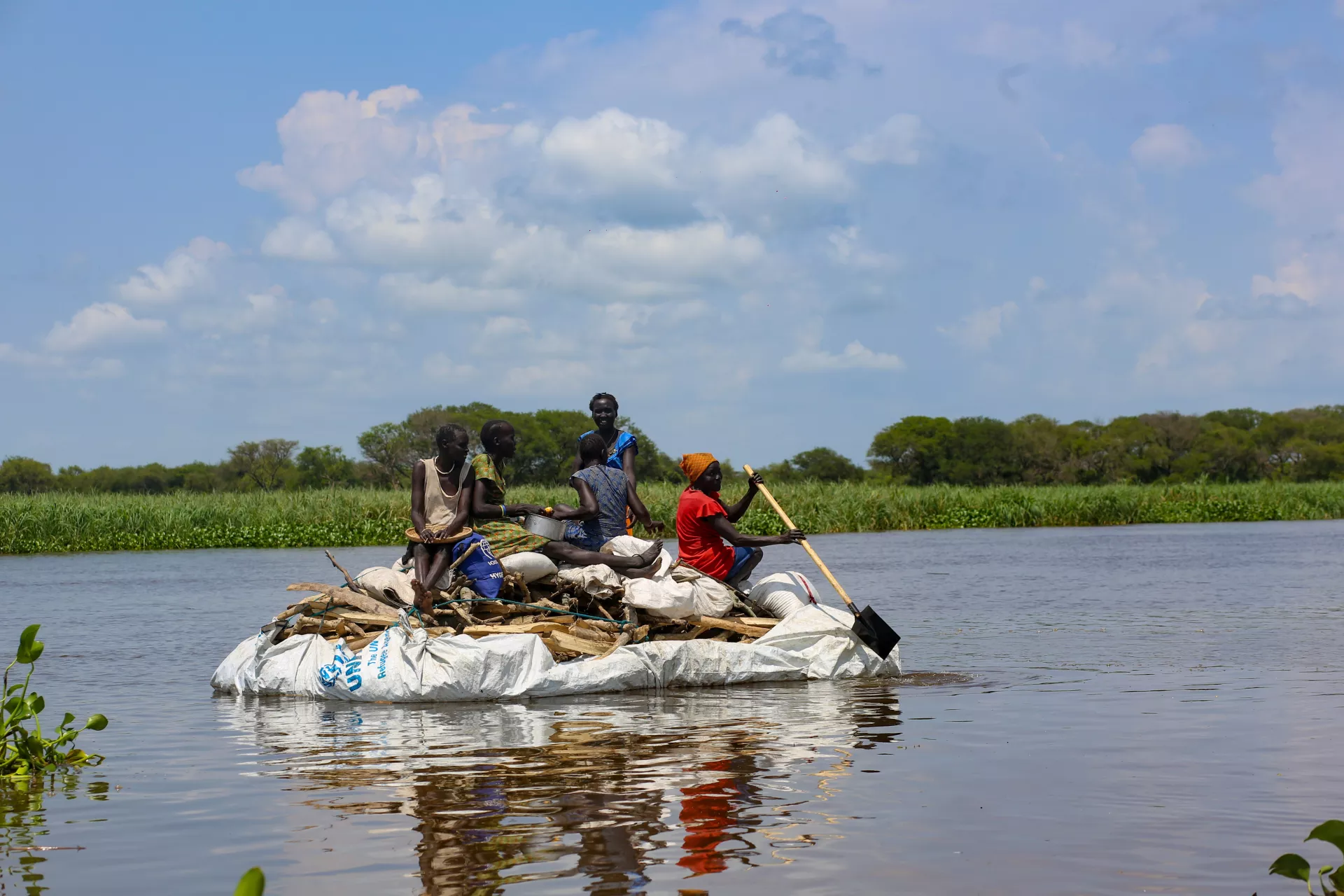 A family has been displaced from their home due floods and are using a tarp to float down the Sobat River to search for dry land.