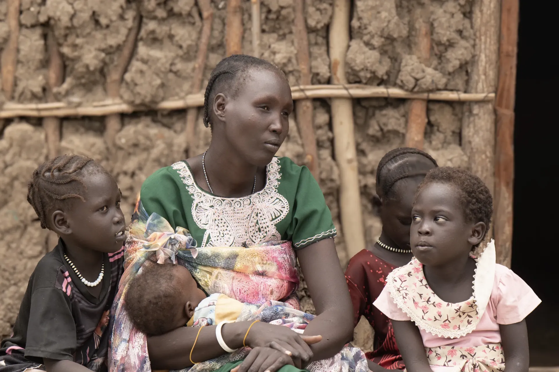 Mother and 4 children. (long, green dress; 4 girls)   Nyageme, 38 years, sits outside her newly constructed house with her four daughters, in the Bor IDP camp. 
