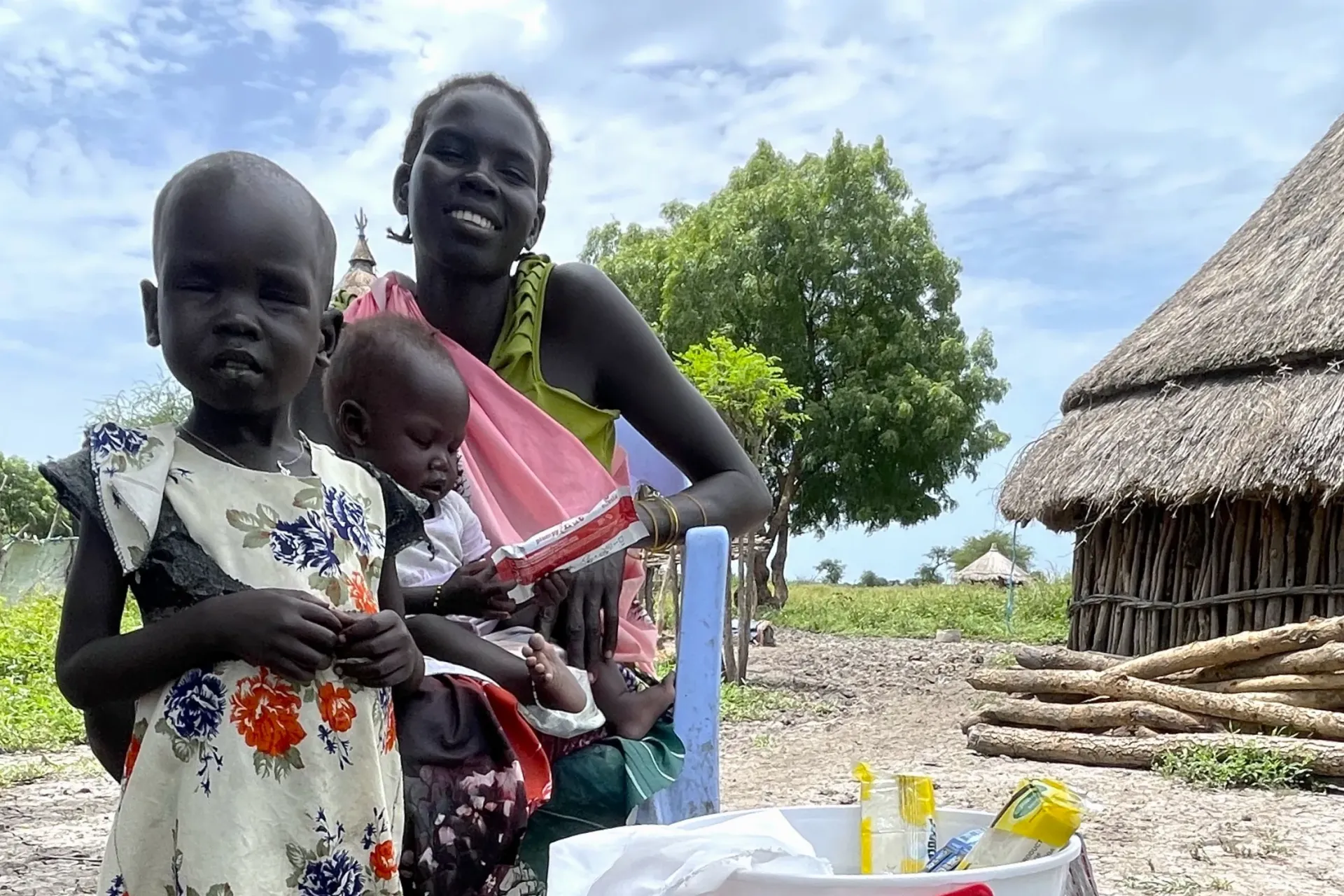Mother is sitting in front of her house holding one of her child with her older child standing in front of her in Akobo, South Sudan