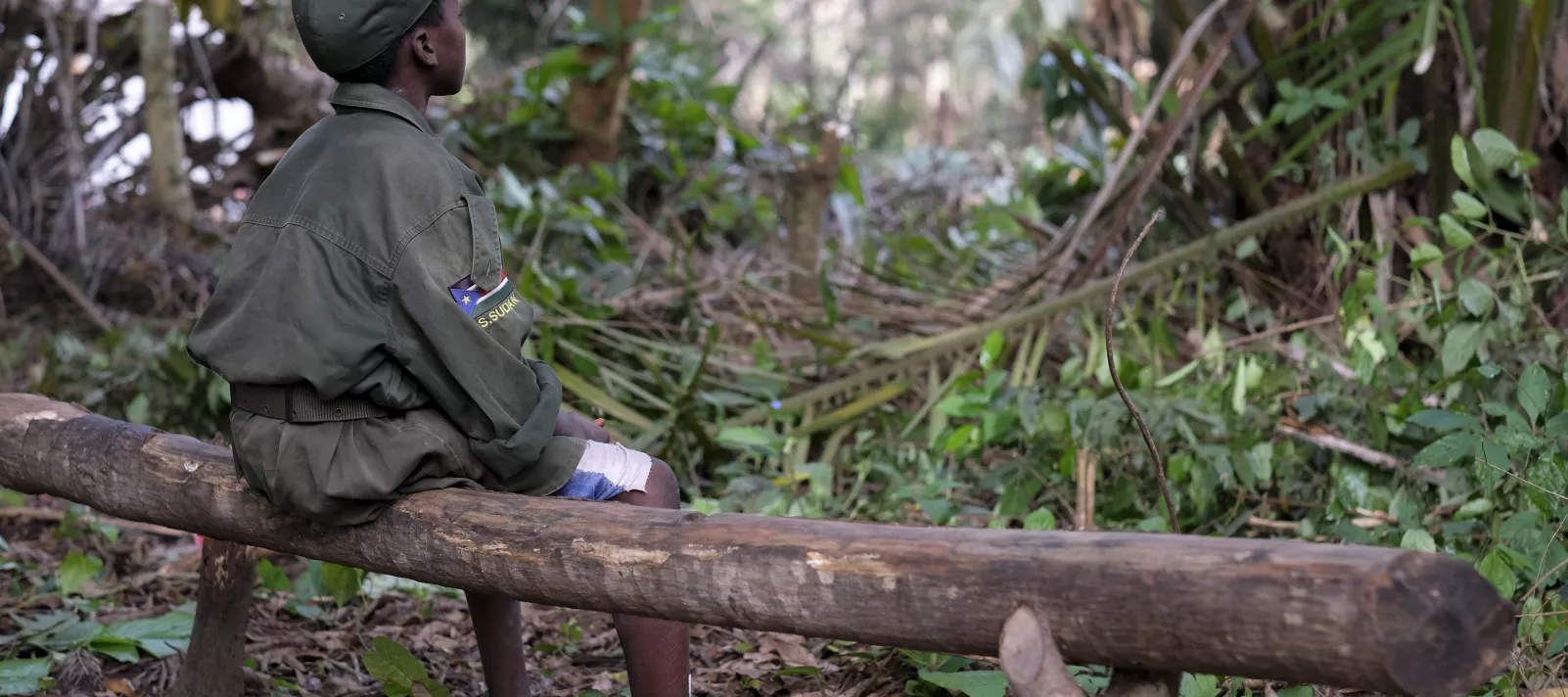 A boy sitting on a log wearing military fatigue