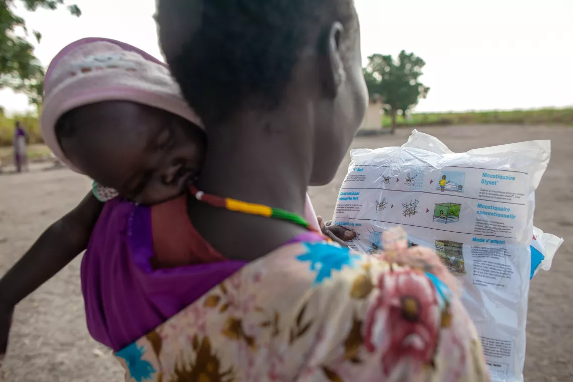 A mother with her sleeping baby on the arm looking at the mosquito net she just received.