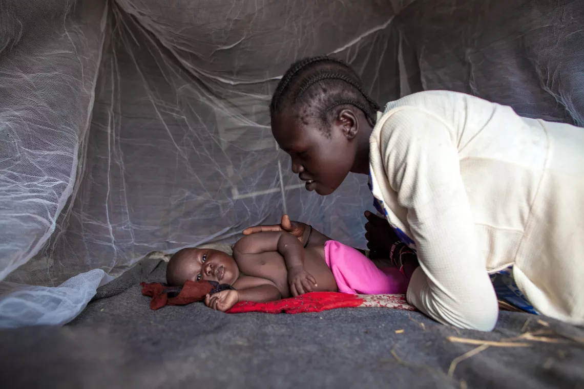 A mother leaning over her child sleeping under a mosquito net