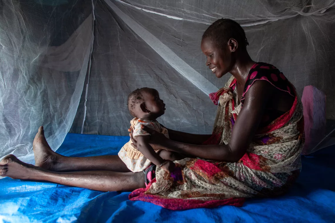A mother sitting under a mosquito net with her child