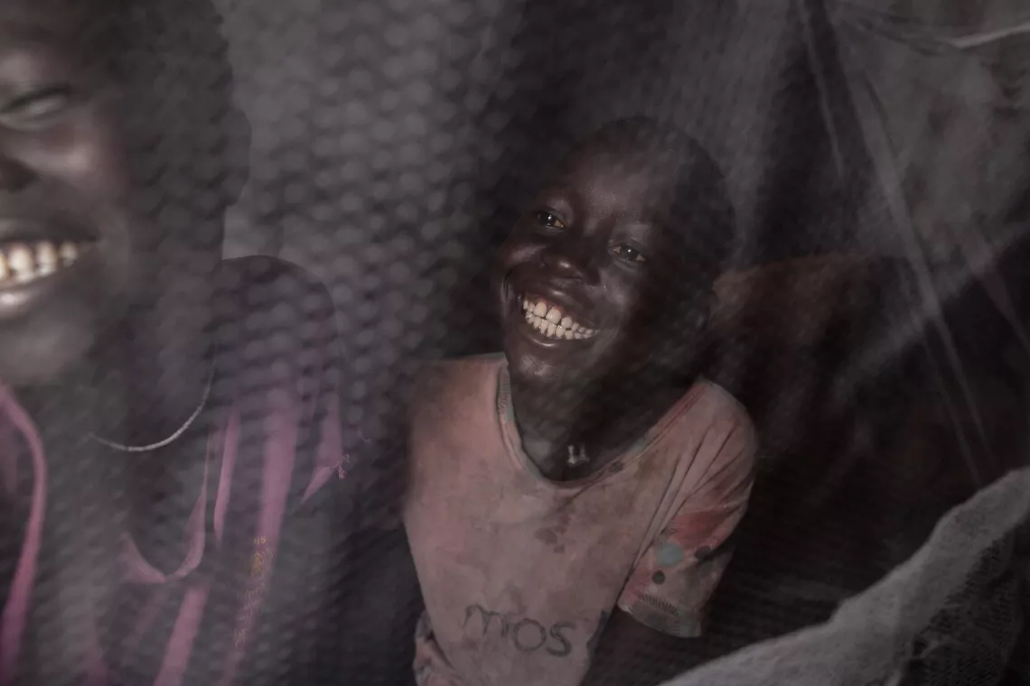 Two children sitting under a mosquito net laughing