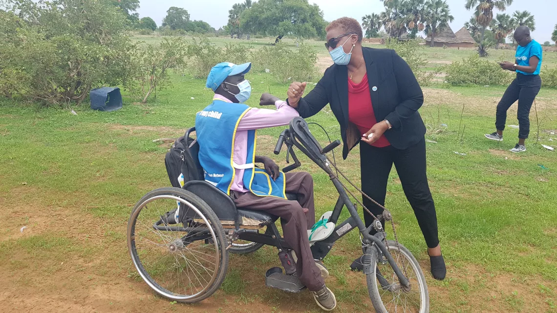 A man seated in a wheelchair is bumping elbows with the UNICEF representative