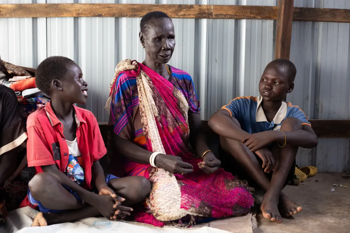 Two twelve year old friends , Jado Joseph (l) , who is a returnee and Aweng Wor, from the host community, listens to Jado&Otilde;s grandmother, Elizabeth Mijok Rup, tell stories at their shelter in the Bulkat transit center, Malakal, on October 27, 2025. 