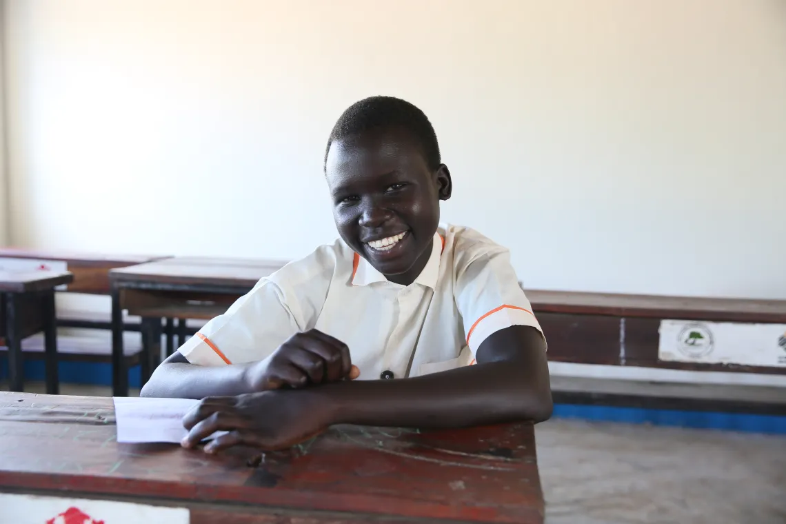 A student girl smiles at the camera while she sit in a new classroom.