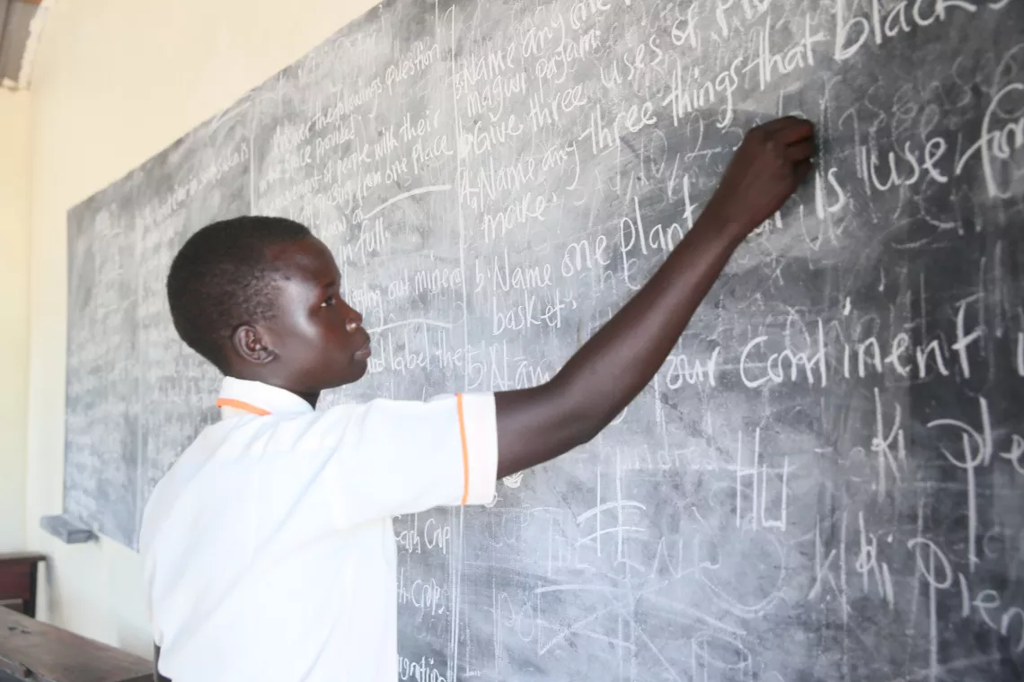 a school girl writes on a blackboard.