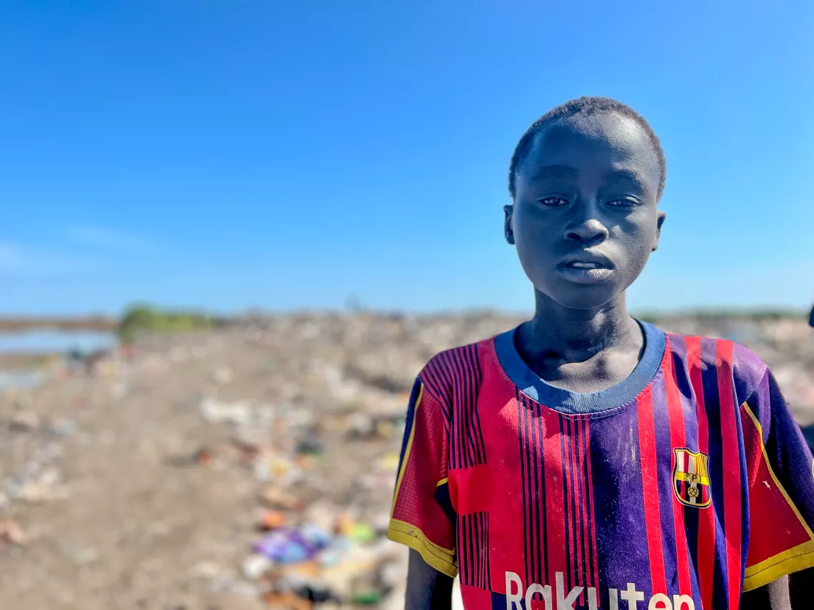 12-year-old Kai stands barefoot in a dumpsite on the outskirts of the Protection of Civilian (PoC) camp in Bentiu