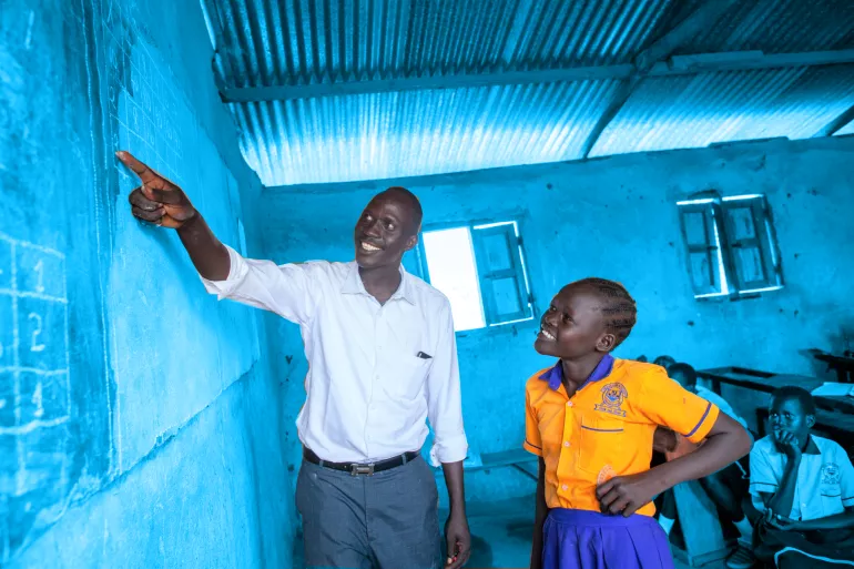 A teacher pointing at the blackboard next to a student