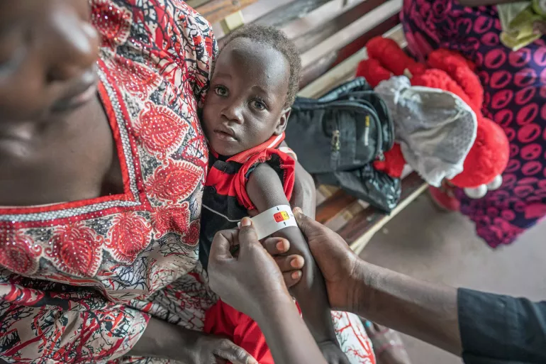 A young child nutritional status is checked with a MUAC tape by a nutrition worker