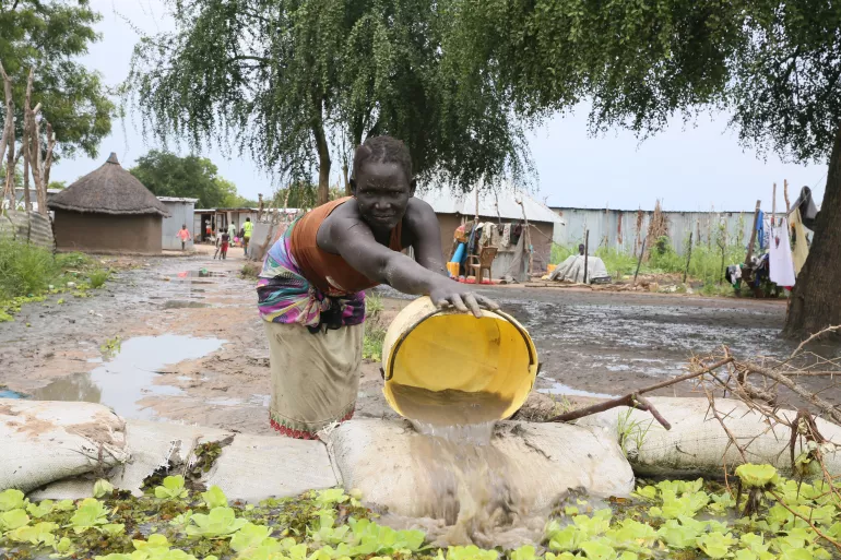 A young girl is bucketing flood water out of her home compound in Bor.