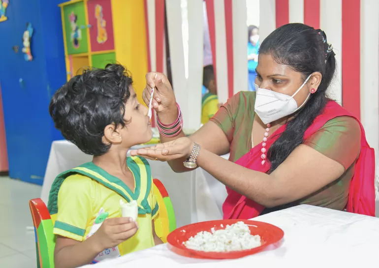 preshool teacher feeding a child