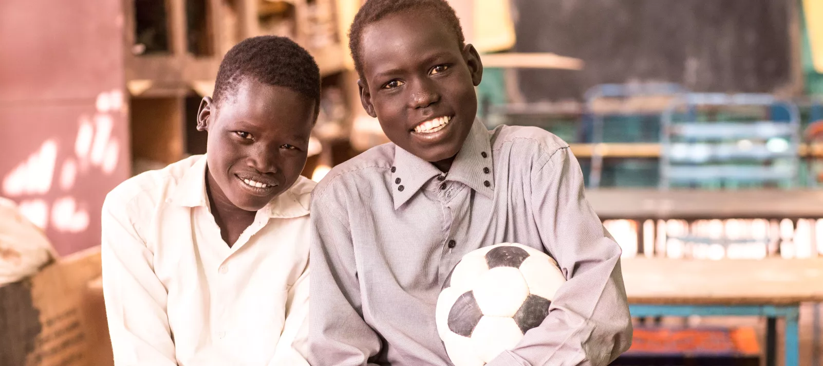 Two boys in a classroom holding a soccer ball