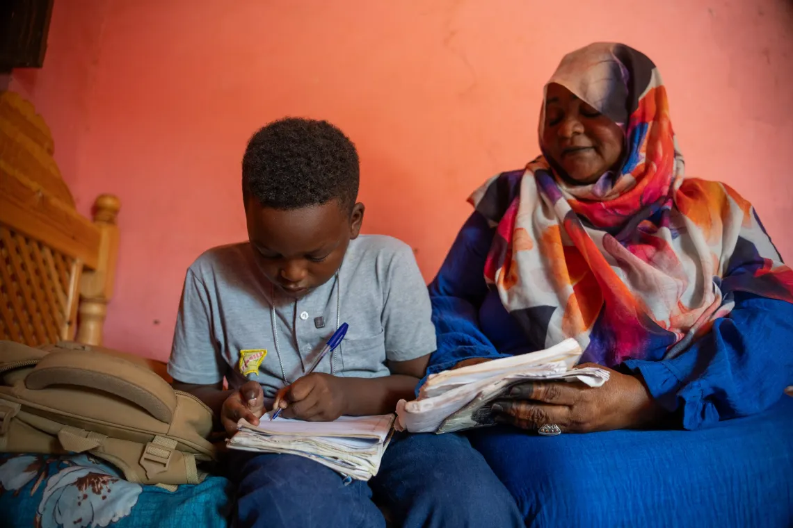 Omer writes his exams as his mother looks on.