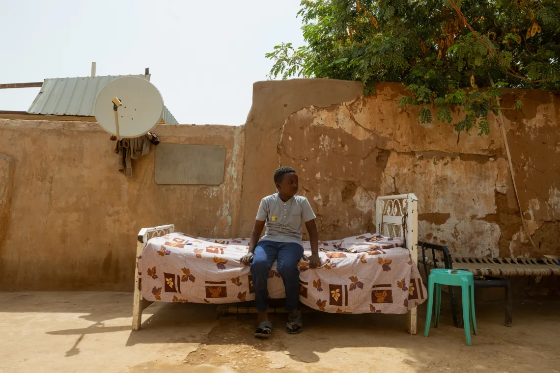 Omer sits on the bed in the home compound.