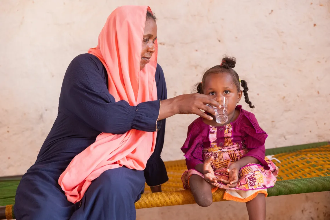 Amera gives water to her 5-year-old Aisha in their home in Khartoum State.
