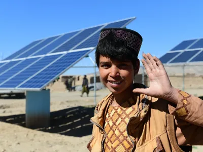 A boy waving his left hand with solar panels in the background.