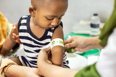 A boy gets his left arm measured with a mid-upper arm circumference (MUAC) measuring tape.