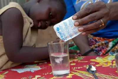Child watches closely as a packet of oral rehydration salts is poured into a glass of water.