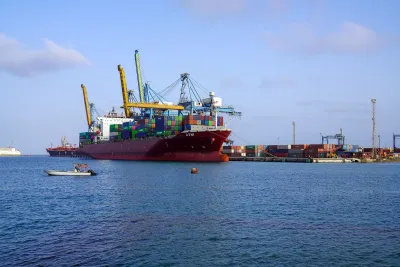 A large cargo ship docked at a port with multiple colorful shipping containers stacked on board and cranes positioned for loading and unloading. 