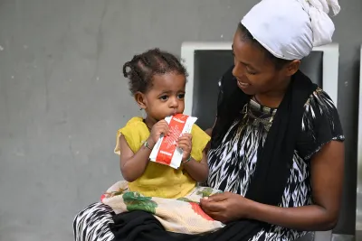 A child on a woman's lap eats ready-to-use therapeutic food (RUTF) from a sachet. 