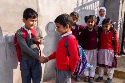 Two boys shake hands while four girls watch them. 