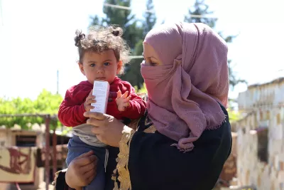 A toddler in the lap of a woman while they hold a package of medicines.