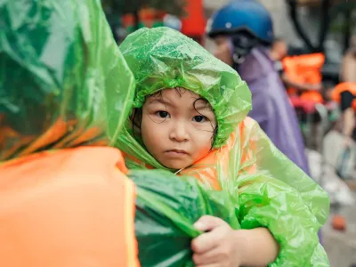 Little girl in raincoat is held by an adult. 