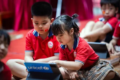 A girl types on a tablet while being watched by a boy.