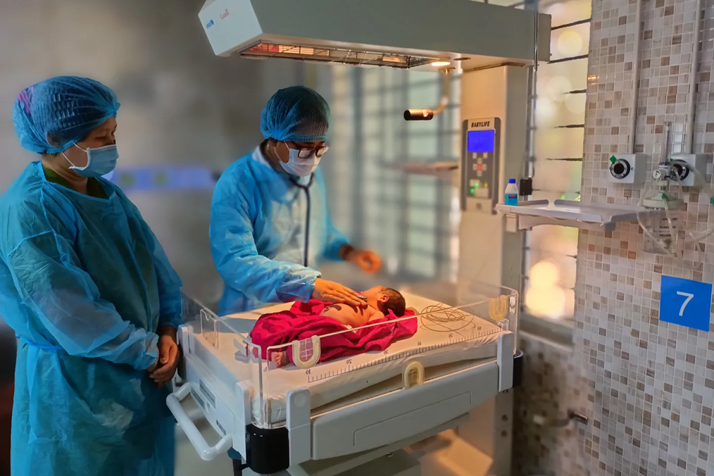 A doctor examines a newborn in a hospital. A nurse is standing next to him. 