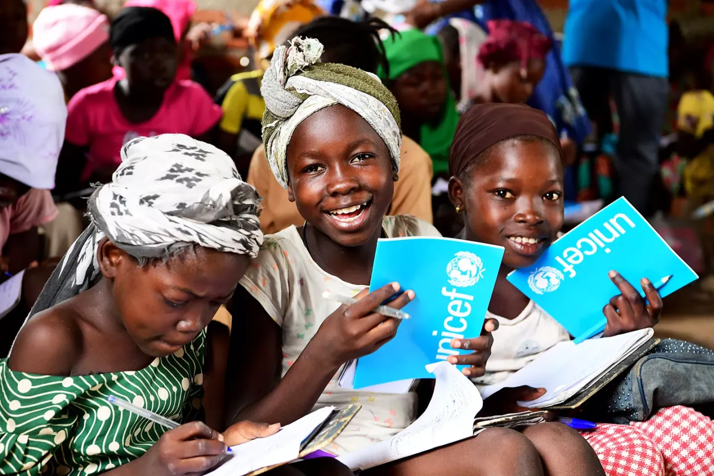 A group of young girls sitting on the floor studying with UNICEF notebooks.
