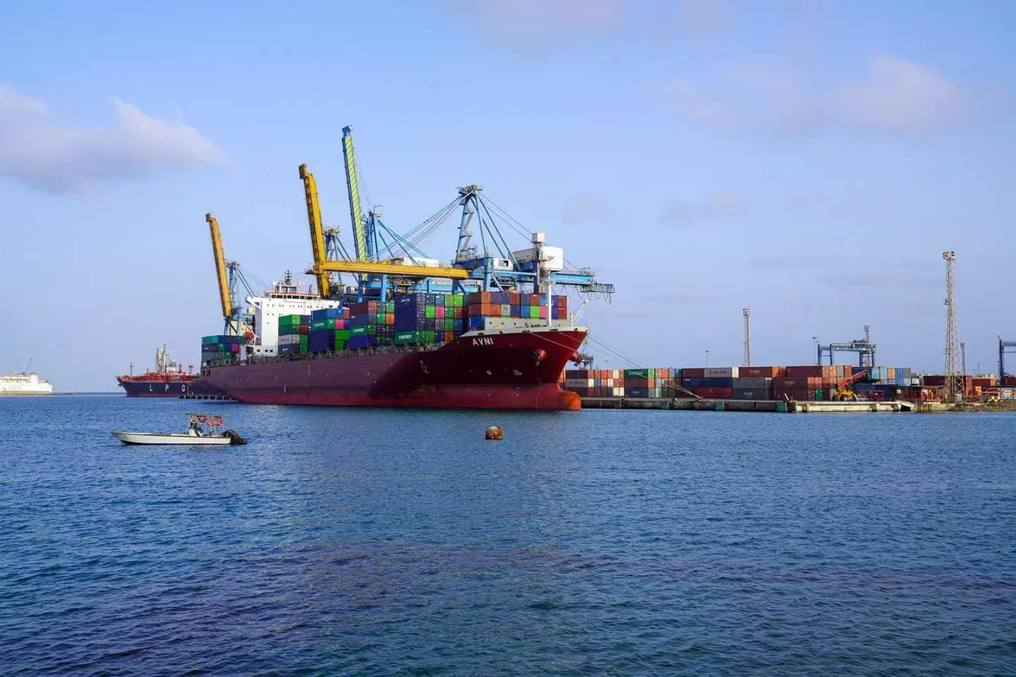 A large cargo ship docked at a port with multiple colorful shipping containers stacked on board and cranes positioned for loading and unloading. 