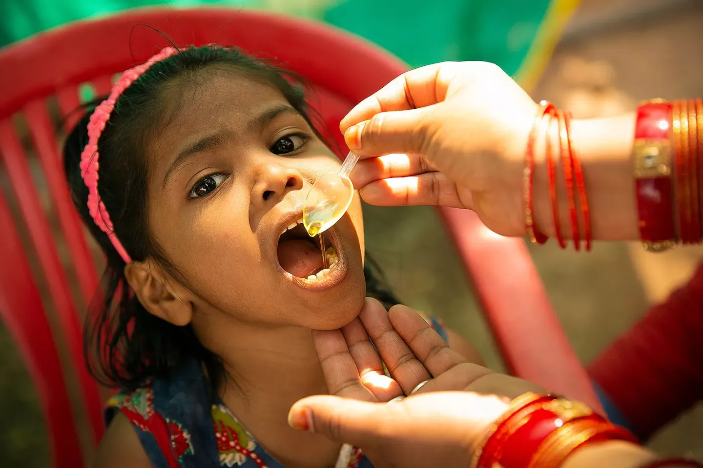 A child girl opening her mouth to receive oral medication in a plastic spoon.