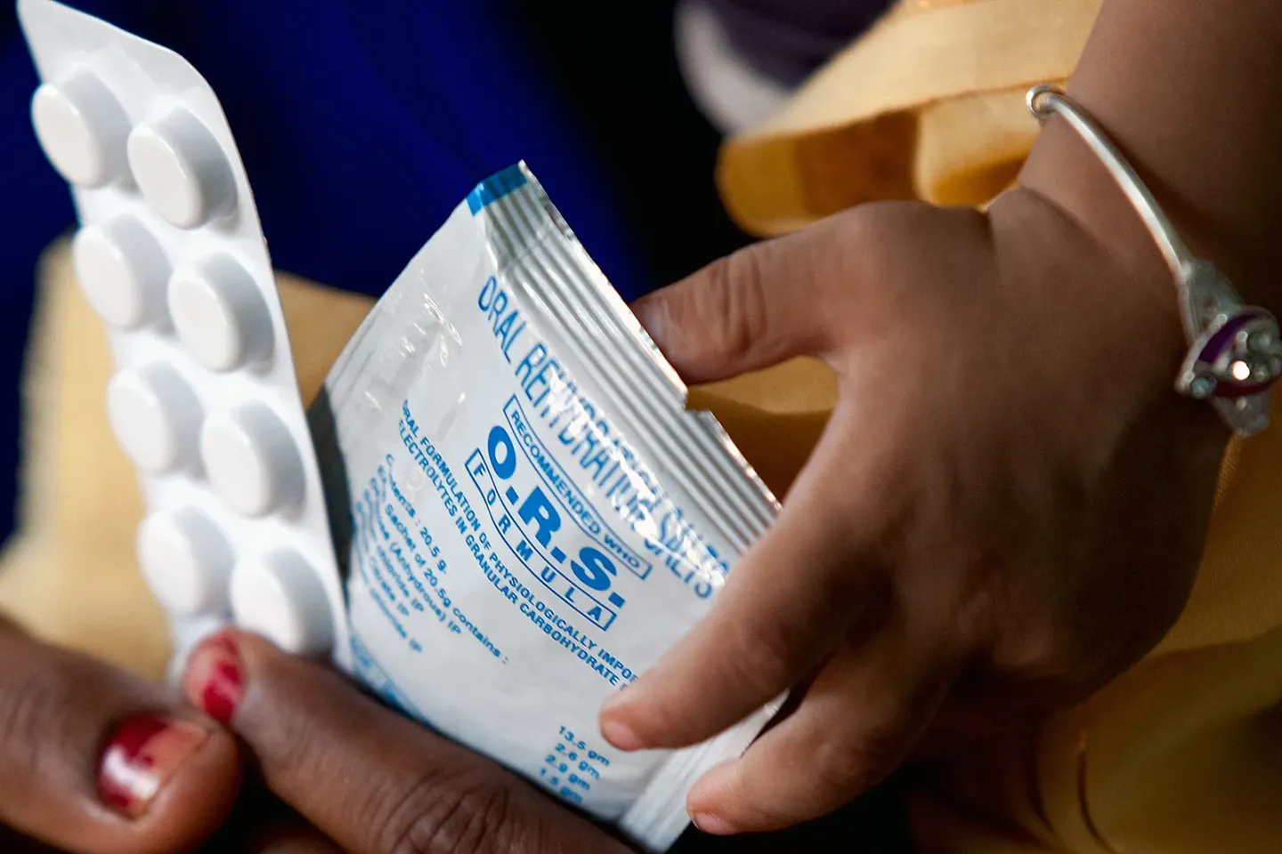 A child and an adult's hands holding an ORS sachet and a blister of zinc tablets.