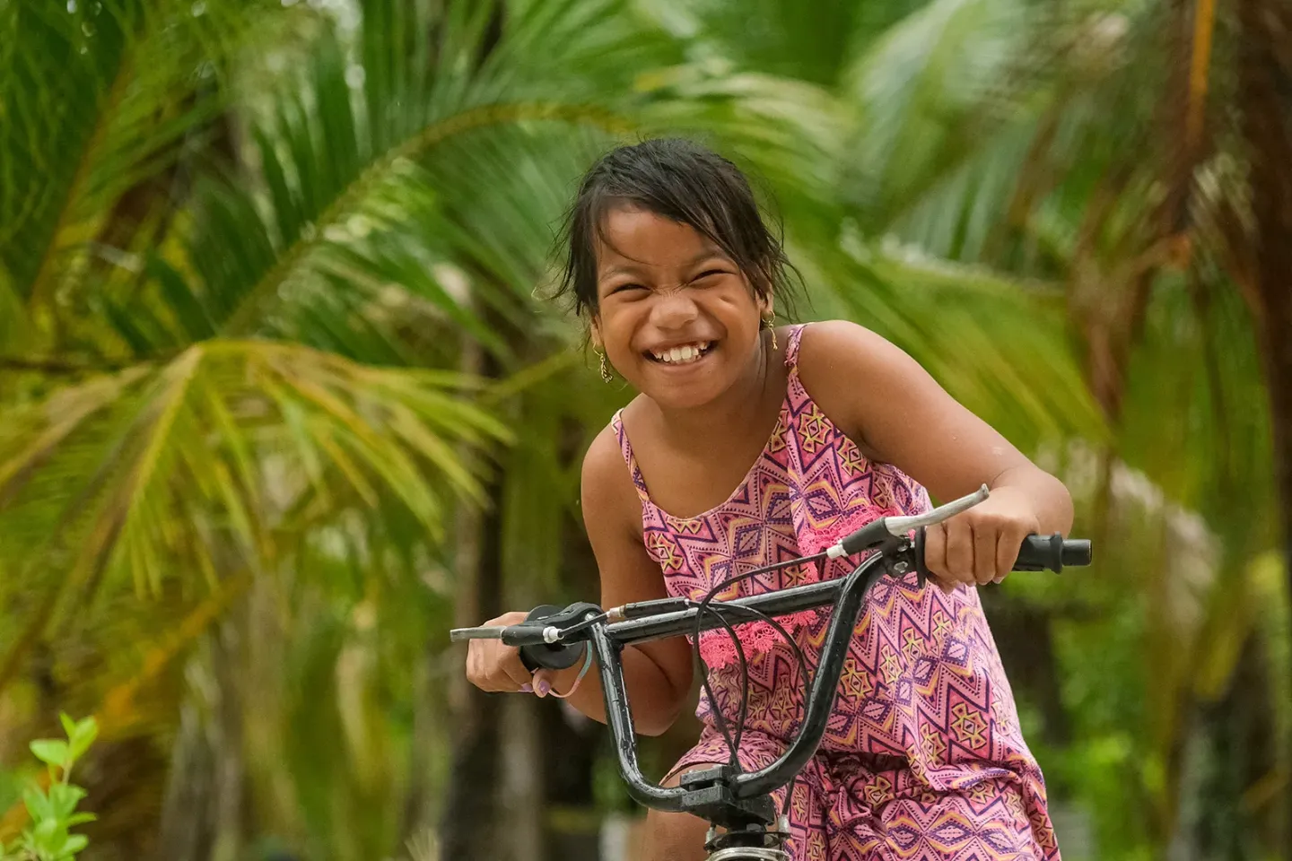 A smiling girl on a bicycle with with tropical palm trees in the background. 