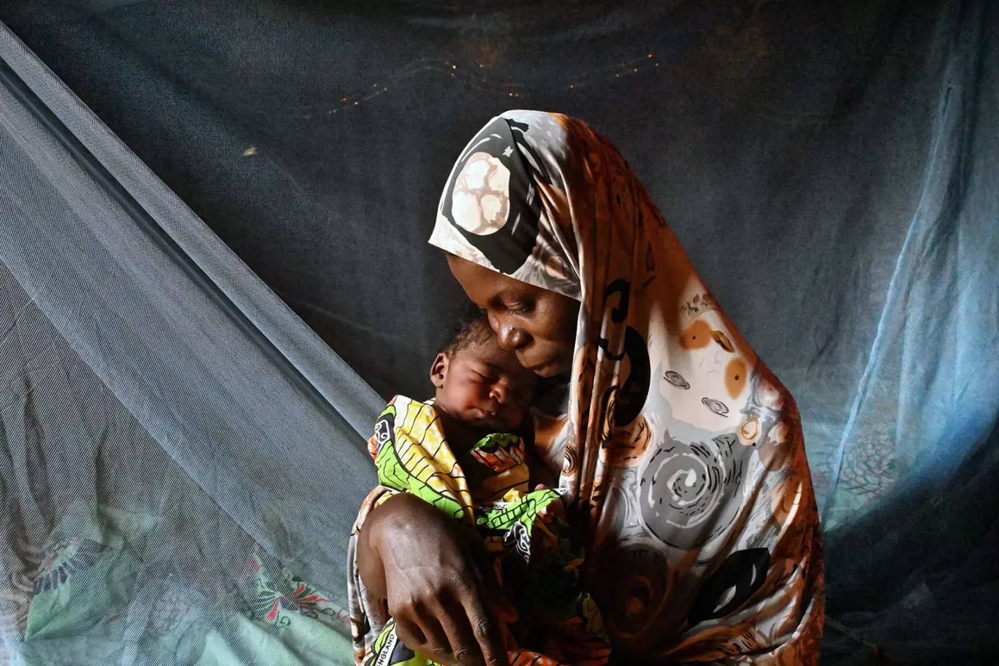A woman holding a newborn under a mosquito net. 