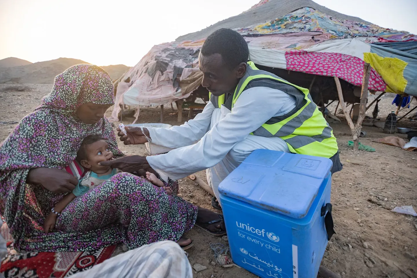Health worker vaccinating a child alongside a vaccine carrier. 