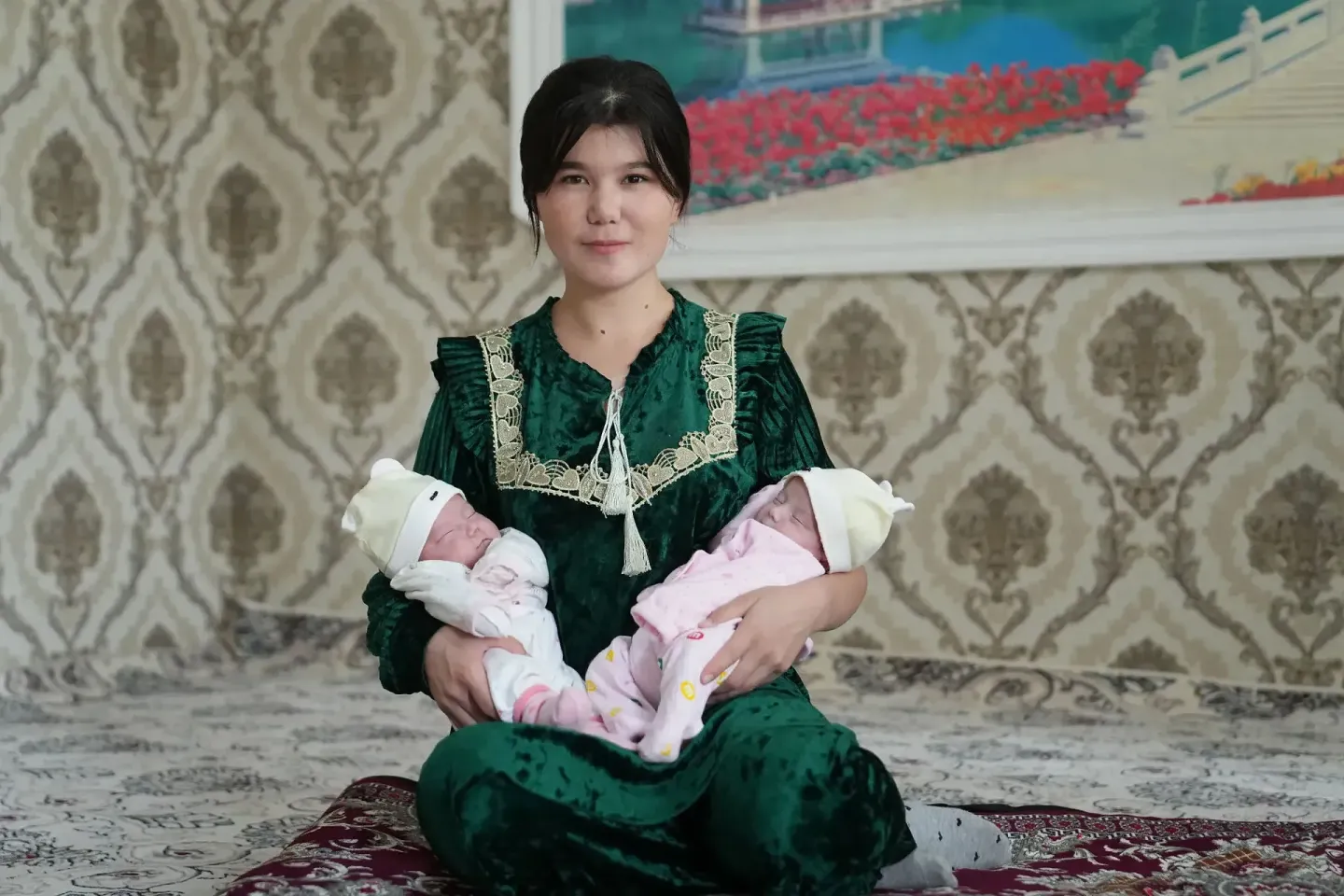 A woman sits while bearing two newborn babies. 
