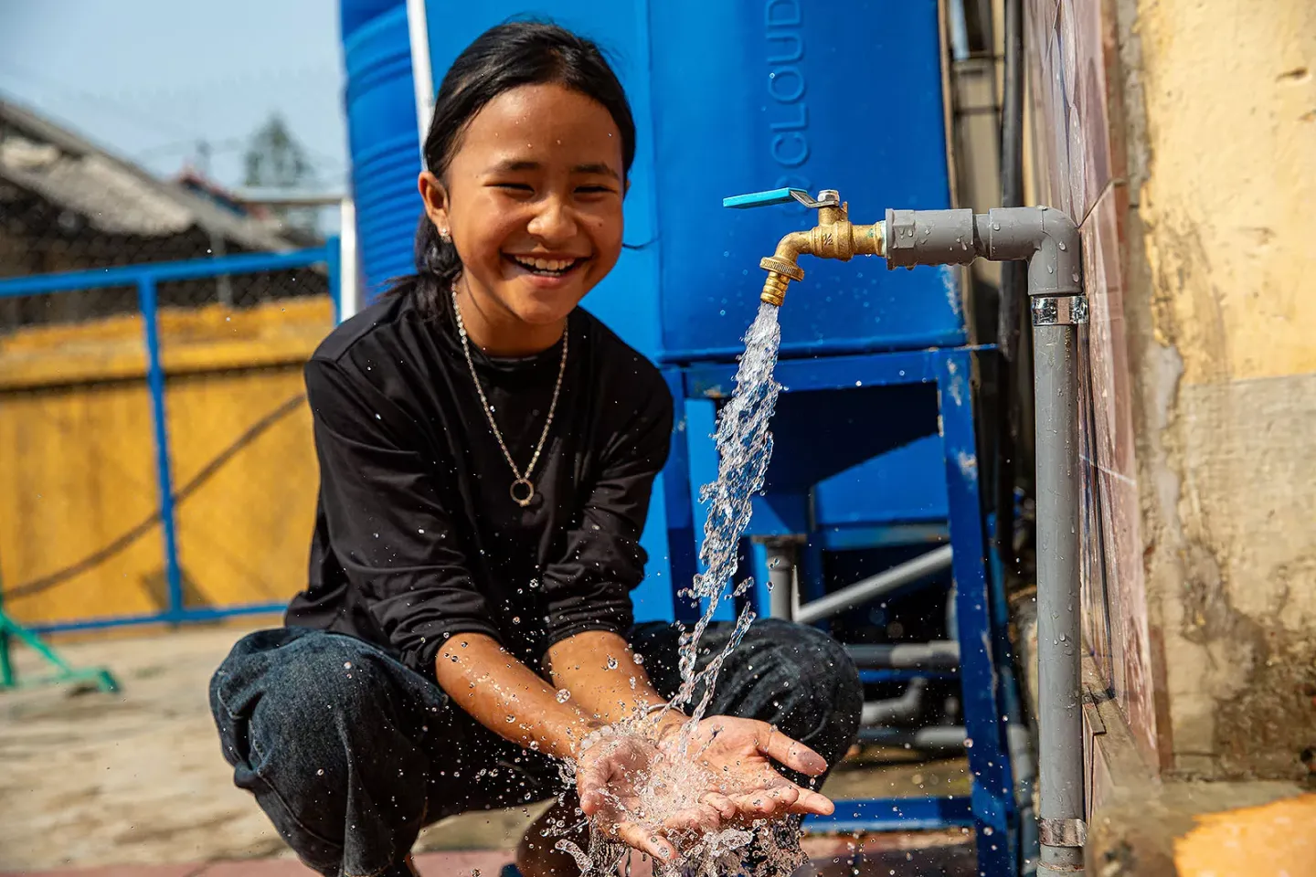 A smilende teenate girl washes her hands at a tap.