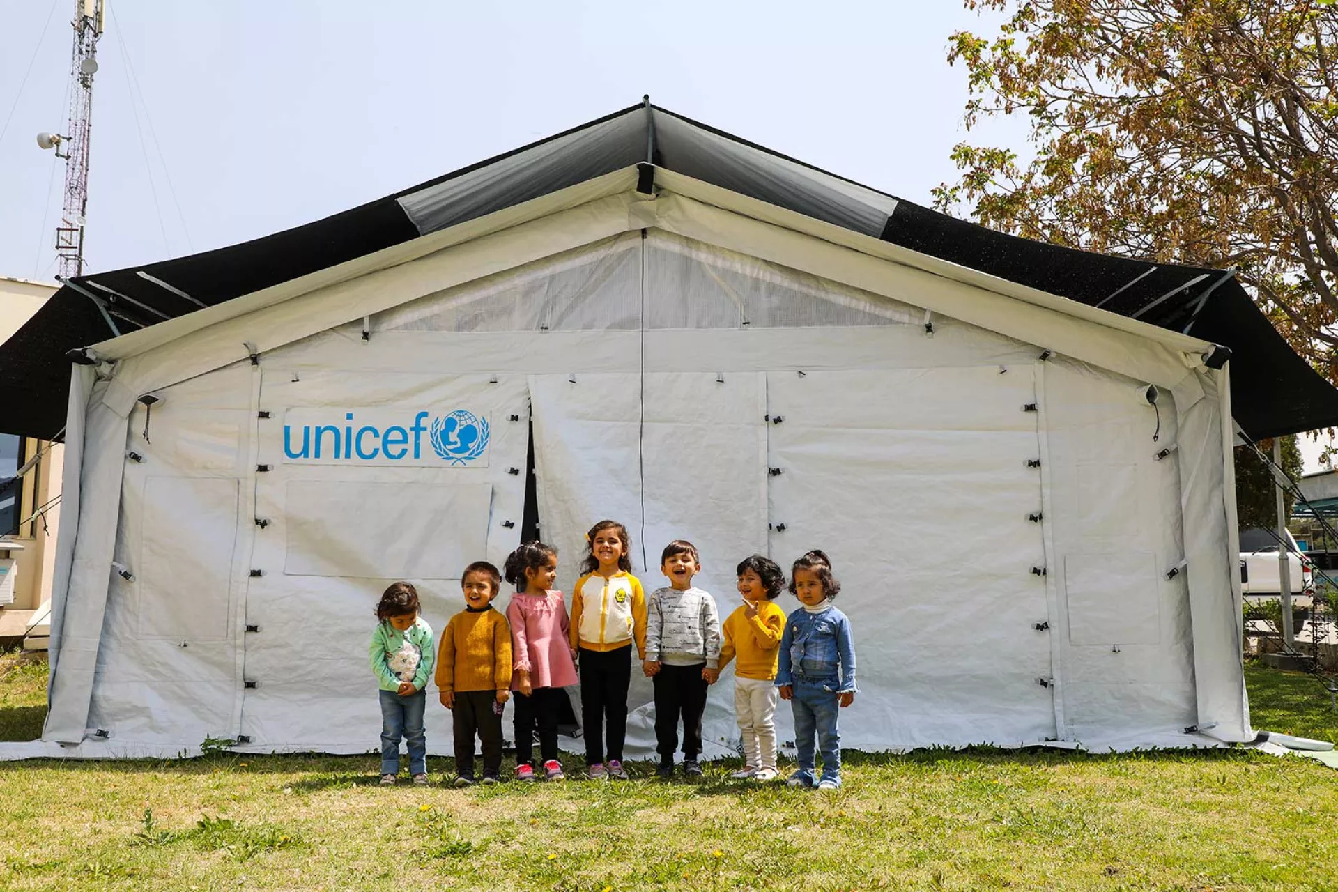 7 children play outside a new High Performance Tent installed in Afghanistan to be used for community based education programmes.