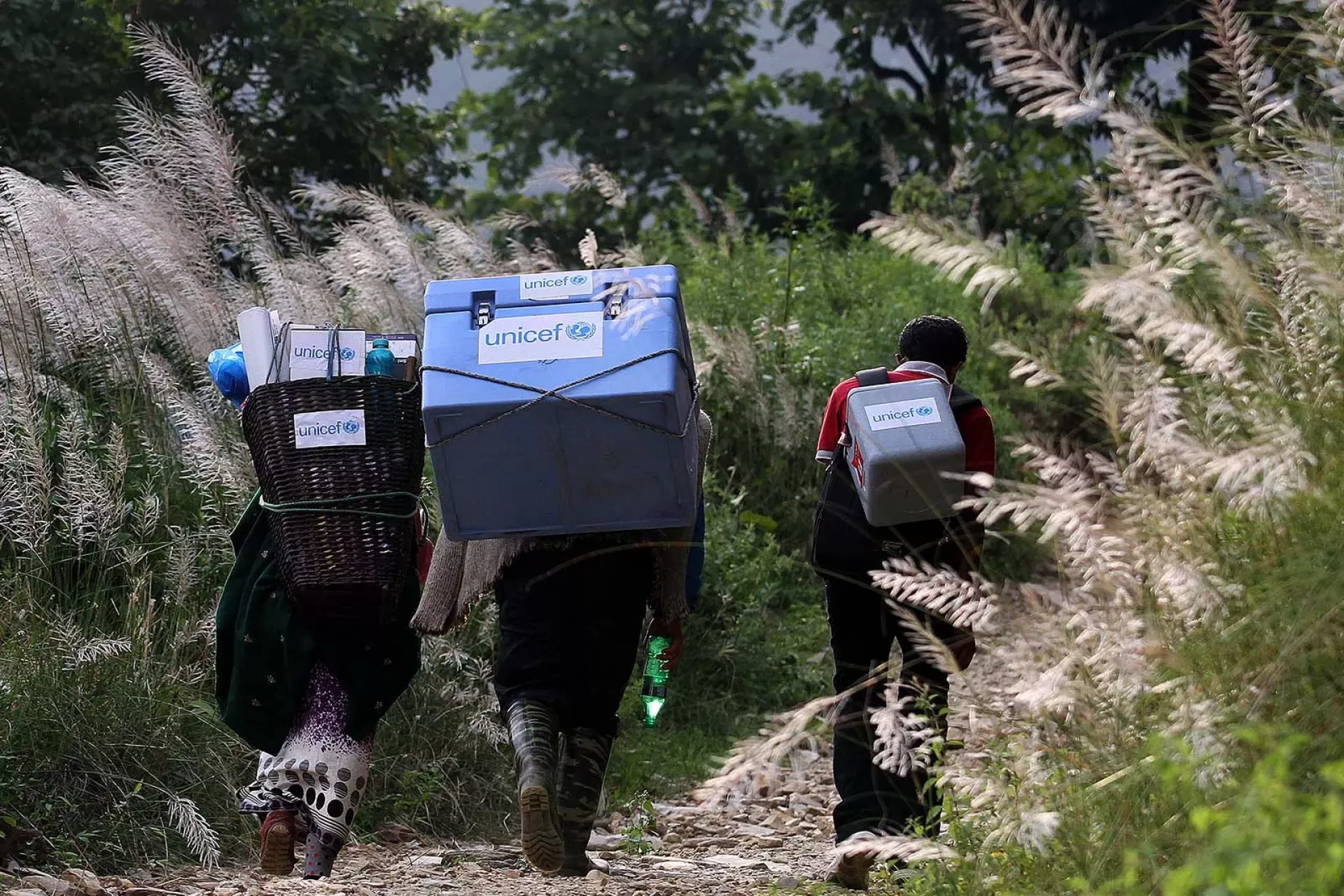 Three people carrying UNICEF-provided vaccines on difficult terrains on the way to a vaccination campaign to be conducted in Gorkha District, Nepal, the epicentre of the 2015 earthquake.