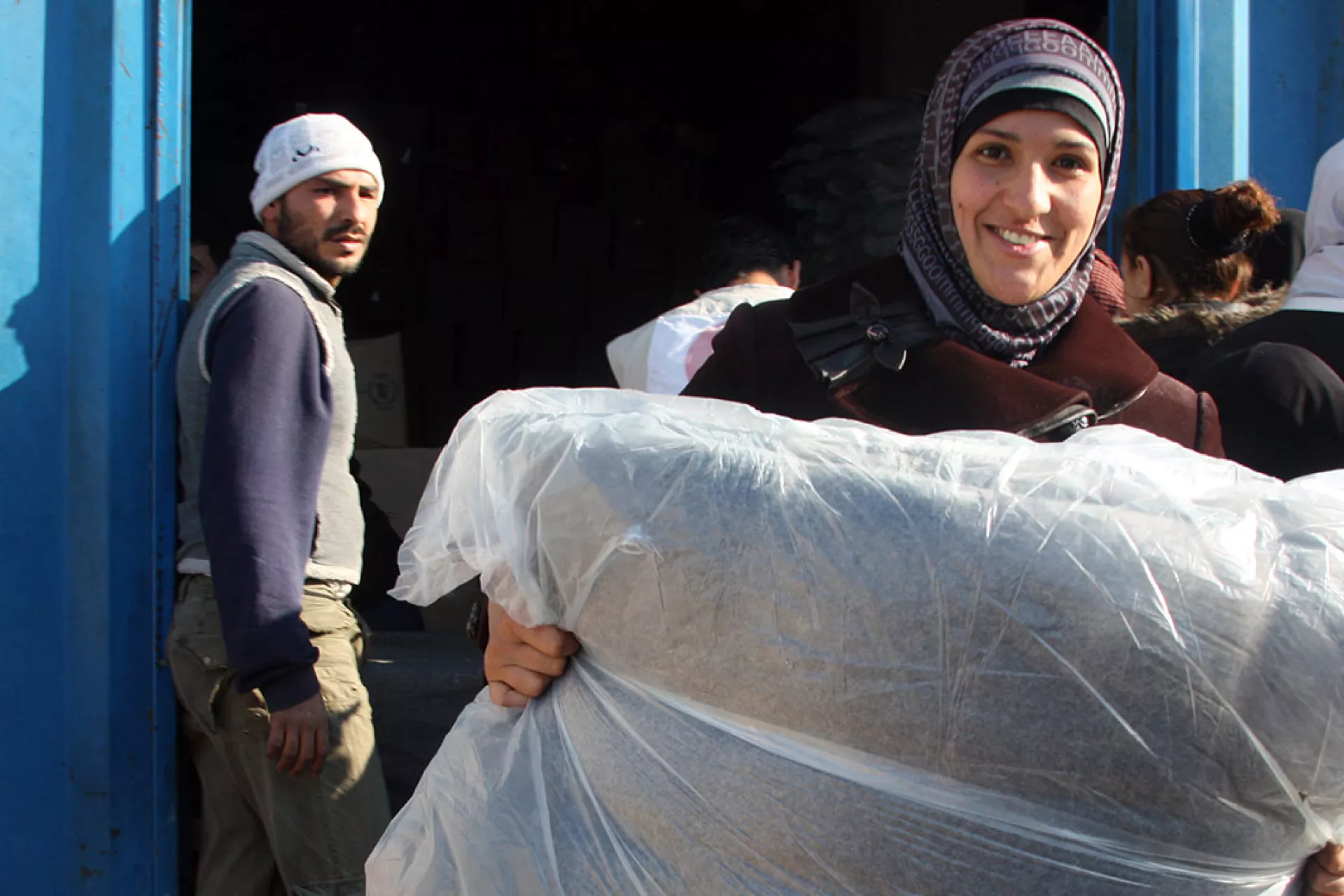 A smiling woman holds UNICEF blankets, among the five she just received during a distribution at a Syrian Arab Red Crescent warehouse, in the city of Lattakia, in December 2013.