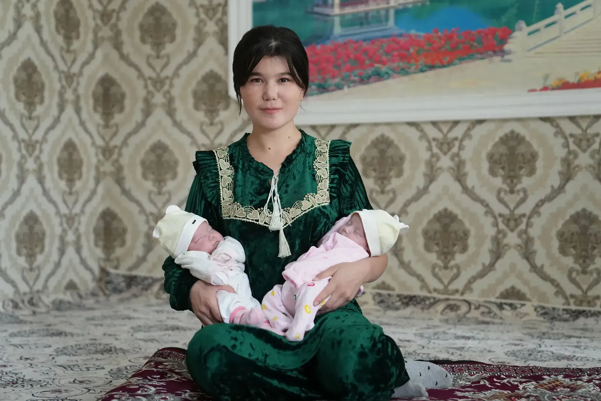 A woman sits while bearing two newborn babies. 