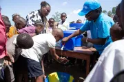 A boy washes his hands with water from a blue plastic container.