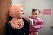 A woman smiles while holds a child in her arms.